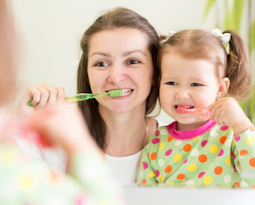 Mother and daughter brushing teeth together happily.